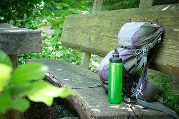  Hiking backpack on wooden bench in the forest, green water bottle with water - 653277971