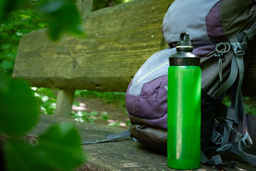  Hiking backpack on wooden bench in the forest, green water bottle with water - 653277987