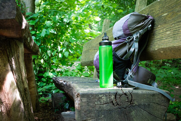  Hiking backpack on wooden bench in the forest, green water bottle with water - 653277993