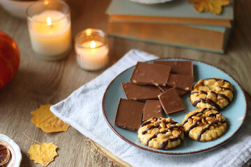 Cup of tea or coffee, plate with desserts, dried oranges, bowl of grapes, scented candles, vintage books, pumpkins and autumn leaves on the table. Autumnal hygge. Selective focus.