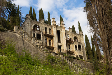 Fototapeta na wymiar The ruins of an abandoned building against the backdrop of cypress trees and blue sky. Stalinist architecture. Legacy of the Georgian-Abkhaz War