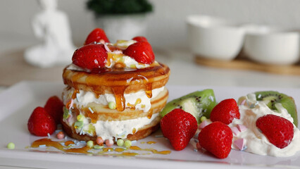 Pouring honey syrup on pancakes. American pancakes with berries and whipped cream on white plate at home. Tasty sweet breakfast food