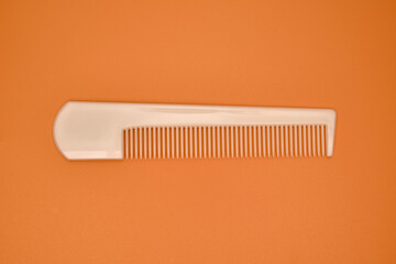 One ivory plastic comb on an orange background