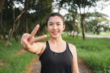 Young Asian woman gives two thumbs up to encourage herself before going for a weight loss run.