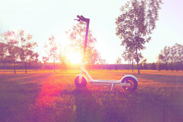 White electric scooter on the lawn.  Scooter in the rays of the sunset.  Environmentally friendly personal transport.  Walking on an electric scooter in nature.
