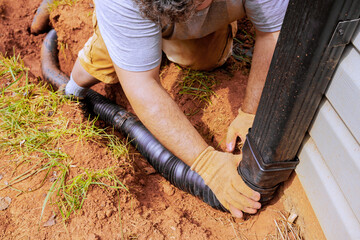 Man installing flexible gutter extension drainage pipe connector downspout with water draining down