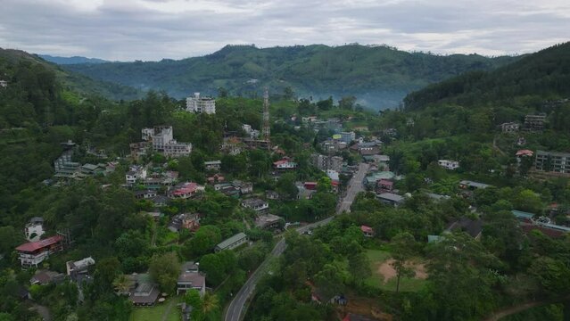 Aerial slide and pan shot of buildings in town in tropical destination. Hilly landscape with lush green vegetation. Ella, Sri Lanka