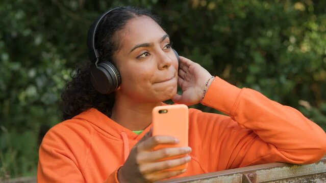 Beautiful mixed race African American girl teenager young woman listening to music on her smartphone or cell phone wearing wireless headphones
