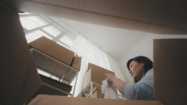 Middle-aged Asian woman unpacking box with clothing, checking quality of t-shirt
