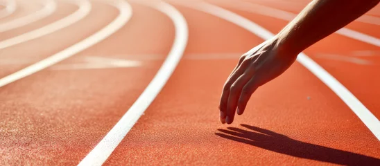 Schilderijen op glas Running track with white lines in stadium. Sport background. Close up of human hand on running track. © Faith Stock
