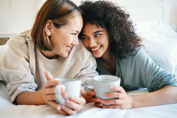 Coffee, love and lesbian couple on bed in conversation for bonding and relaxing together. Happy, rest and interracial lgbtq women laughing, talking and drinking latte in bedroom of modern apartment.