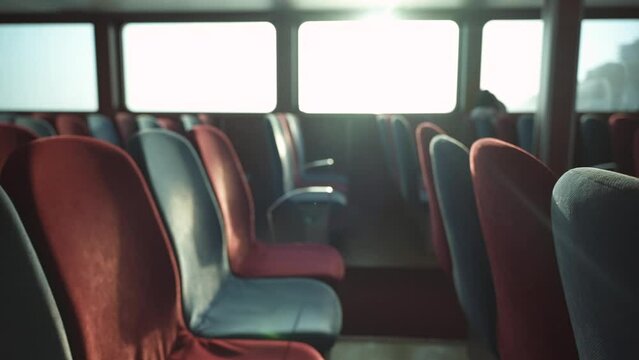 Slow motion along rows of empty passenger seats inside the ferry ship. The sunset sun shines through the windows. The capacity of municipal transport