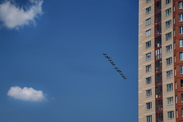 Group of army air force demonstrates aerobatics. Military aviation victory parade over city multi-storey buildings. Presentation of aviation equipment in blue sky against background of clouds.