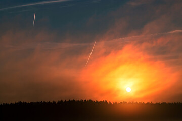 Obraz premium Sunrise over the forest. Beautiful sky with traces of airplanes