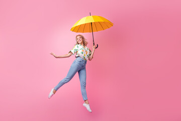 Full length photo of charming shiny lady jumping running bring her yellow umbrella flying light...