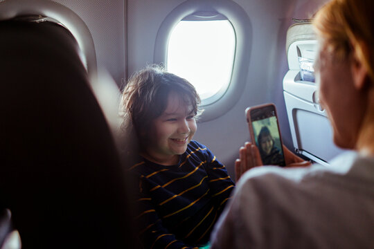 Young mother taking a picture of her son on a smartphone on their flight