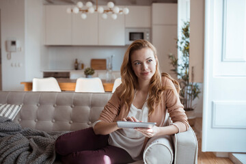 Young redhead woman using the tablet on the couch at home