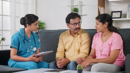 Indian nurse advising or counseling middle aged couple during routine health check up or home visit - concept of home medical advice, encouragement and medicare service.