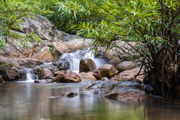A small waterfall with many rocks in the stream. Surrounded by trees in the mountain forest.