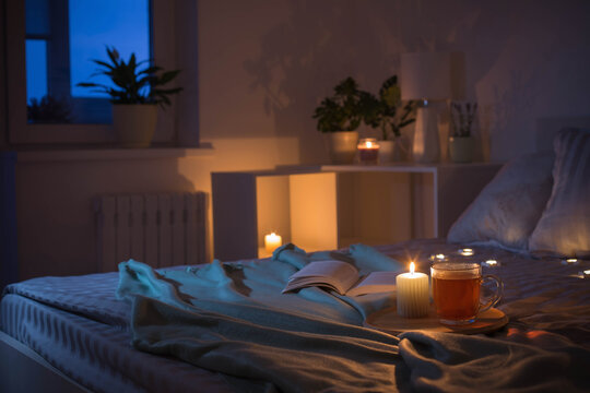 cup of tea with burning candle on wooden tray on bed in bedroom in evening