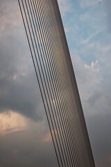 A suspension bridge's main cable, consisting of numerous smaller cables, stretches diagonally across the overcast sky.