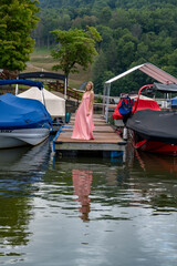 Pretty young girl at marina standing on the dock in pink dress.