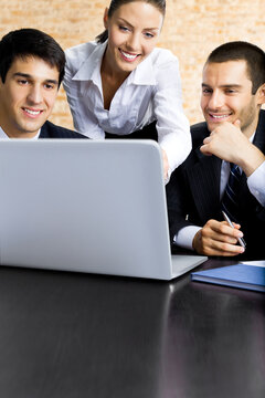 Three happy smiling successful business people working with laptop at office.  Brown bricks wall background.