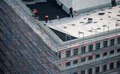 Birdseye view of roofer waterproofing the flat roof of a commercial building.