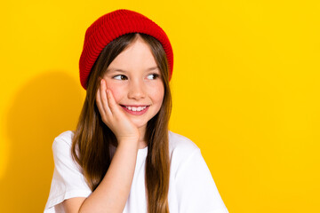 Photo portrait of adorable small girl touch cheek look empty space wear trendy white outfit isolated on yellow color background