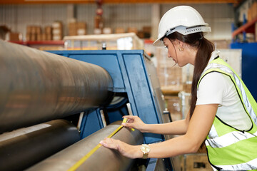 female factory worker using tape measure and measuring the length of the steel pipe in the factory