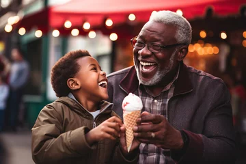 Fotobehang Cheerful black grandfather and grandchild eating ice cream outdoors on sunny summer day. Granddad sharing a dessert with a child in outdoor cafe. © MNStudio