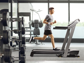 Fototapeta na wymiar Full length profile shot of a guy training on a treadmill