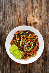 Asian food - roast beef, noodles and stir fried vegetables on wooden table
