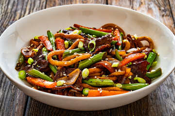 Asian food - roast beef, noodles and stir fried vegetables on wooden table
