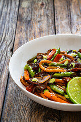 Asian food - roast beef, noodles and stir fried vegetables on wooden table
