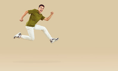 Fototapeta na wymiar Energetic teenage boy joyfully running and jumping in hurry to catch crazy discounts. Stylish guy running near copy space, isolated on beige background. Concept of discounts on goods for teenagers.