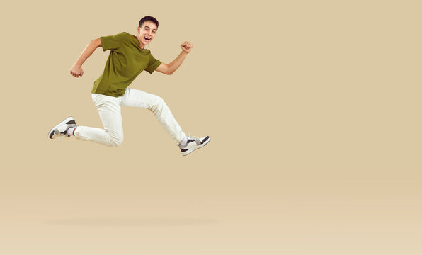 Energetic teenage boy joyfully running and jumping in hurry to catch crazy discounts. Stylish guy running near copy space, isolated on beige background. Concept of discounts on goods for teenagers.