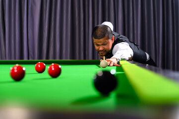 Asian snooker player while aiming to white ball shoot to hit the Snooker ball in game on snooker...
