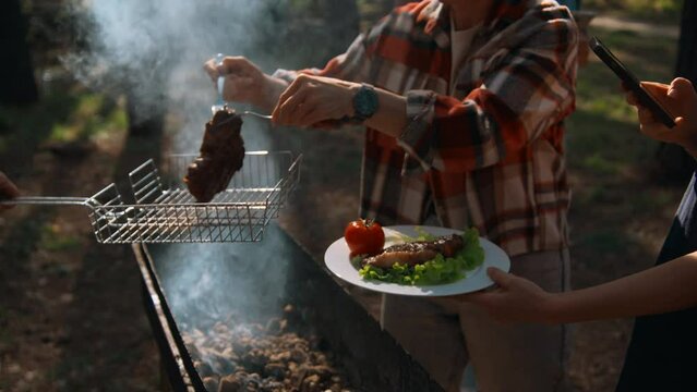 Picnic in nature in the woods BBQ over a campfire with smoke. Stock footage. Man putting delicious chicken into the woman plate with vegetables.
