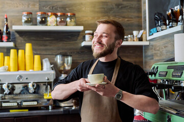 Portrait of barista male in an apron with freshly prepared cappuccino coffee - Powered by Adobe