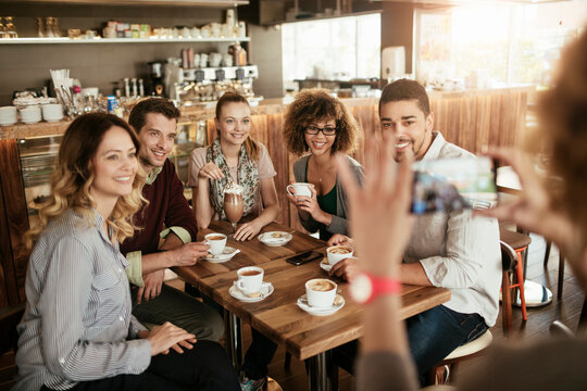 Group of young and diverse friends getting their picture taken on a smartphone while having coffee together in a cafe or bar