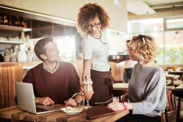 Young African American waitress serving coffee to a Caucasian couple at the cafe or bar