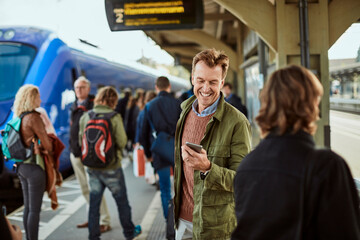Middle aged man using his smartphone while waiting for the train at the train station