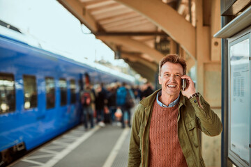 Middle aged man talking on his smartphone while waiting for the train at the train station