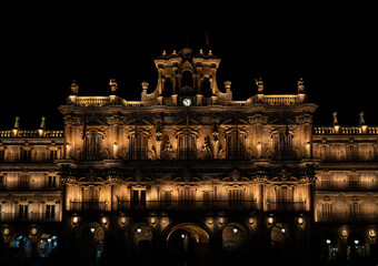 Obraz premium Salamanca City Hall at night, dimly and beautifully illuminated by orange lights that illuminate the wooden windows, sculptures and the clock.