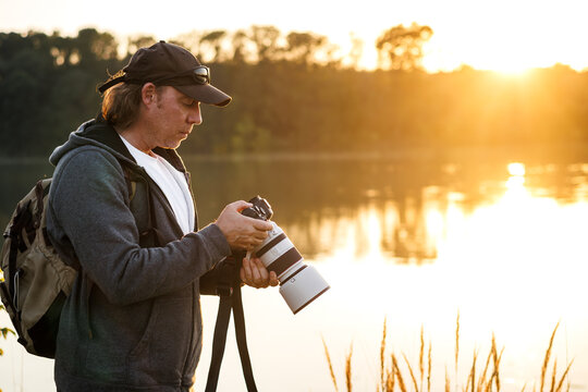 Landscape and wildlife photographer looks at photos on camera screen that he took at lake at sunset