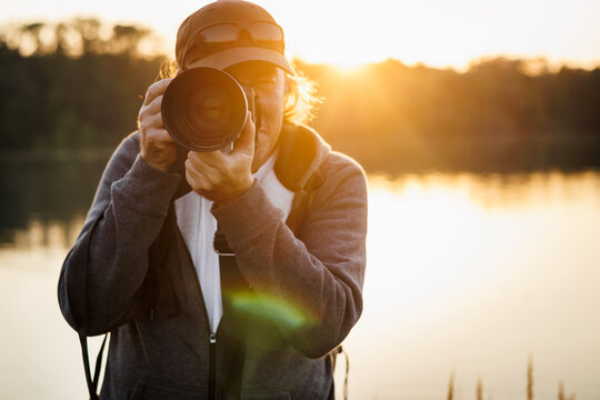 Fototapeta Wildlife photographer with camera photographing nature on lake at sunset. Front view of man, selective focus at lens