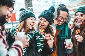 Fototapeta premium Happy friends having fun drinking mulled wine and hot chocolate at Christmas Market - Cheerful young people enjoying winter holidays on weekend vacation - Tourism lifestyle and friendship concept