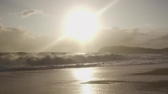 Spiaggia del Mingardo avvolta da una luce dorata, con il sole e Capo Palinuro all'orizzonte e il mare agitato