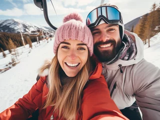 Schilderijen op glas Portrait of happy couple on a gondola at a ski resort make selfie , snowy mountain landscape on background. © Julija